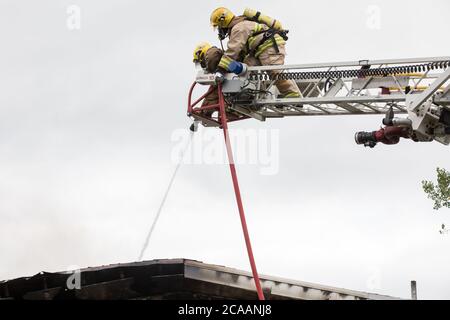 Firefighters spray water on roof with hose from ladder. Stock Photo