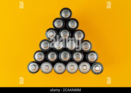 Top view of used batteries arranged in a triangle shape isolated on a yellow background Stock Photo