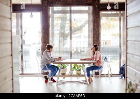 Panoramic view of big spacy room and caucasian couple sitting opposite at the same table in the house with big windows over background. Copy space. Stock Photo