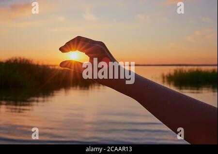 child is taking the sun in one hand, trying to catch it in front of the lake Chiemsee during sunset Stock Photo
