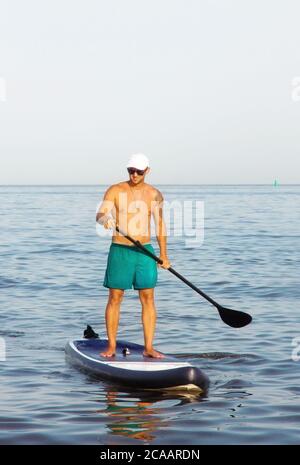 Man is training on a SUP board in the summer sea at sunny day. Stock Photo