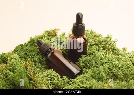 Two brown serum glass bottles with pipette on the green moss. Natural Organic Spa Cosmetic concept. Front view.