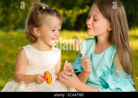 sisters with sweet lollipops in nature in the summer in the park Stock Photo