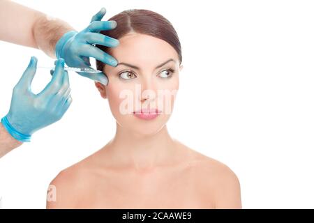 Woman having anti wrinkles, anti-aging serum shot around eyes plastic surgery done by doctor's hand in blue gloves holding injection over woman's face Stock Photo