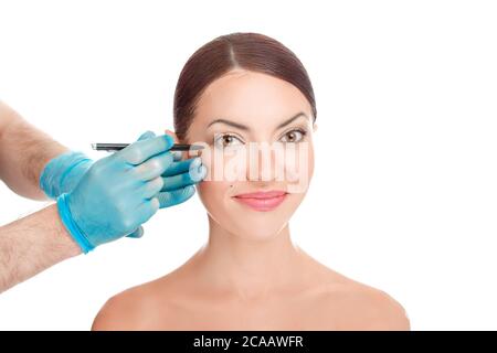 Plastic surgeon about to draw surgery line under eye of girl. Hand in blue glove holding pencil. Plastic surgery, beauty portrait, closeup  isolated o Stock Photo