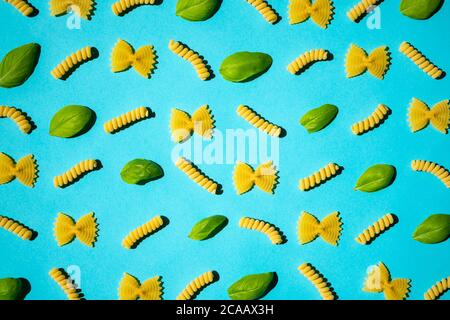 Uncooked curly pasta and basil leaf pattern on blue background. Traditional dry raw macaroni pattern. Nobody Stock Photo