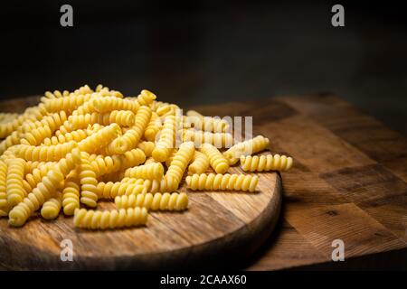 Uncooked curly pasta on wooden table background. Stack of traditional dry raw macaroni. Nobody Stock Photo