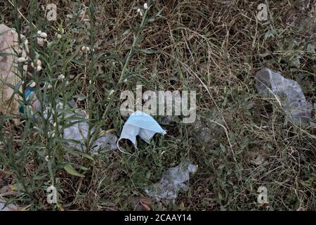 Plastic garbage and covid-19 masks among the undergrowth of an abandoned field near the city Stock Photo
