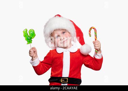 A child boy 4 years old in a New Year costume and a hat of Santa Claus holds candies in his hands. Cheerful positive joyful concept about holidays and Stock Photo