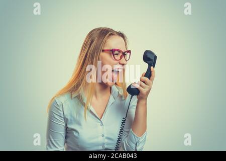 Young woman in glasses holding telephone receiver and yelling with anger Stock Photo