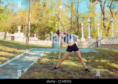 Slim sportive woman training on meadow in beautiful autumnal park doing side bends Stock Photo