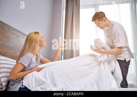 dissatisfied with family life, husband and wife quarrel in bed, man hold blanket in hands, scream at woman, disagreement Stock Photo