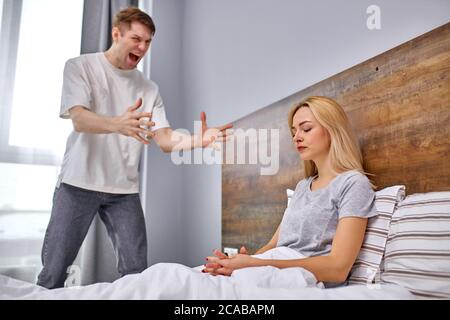how much one can sit offended,do the housework dissatisfied man want her lazy wife to do housework, offended woman sits on bed Stock Photo