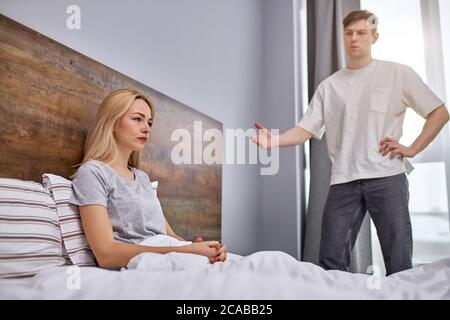 how much one can sit offended,do the housework dissatisfied man want her lazy wife to do housework, offended woman sits on bed Stock Photo