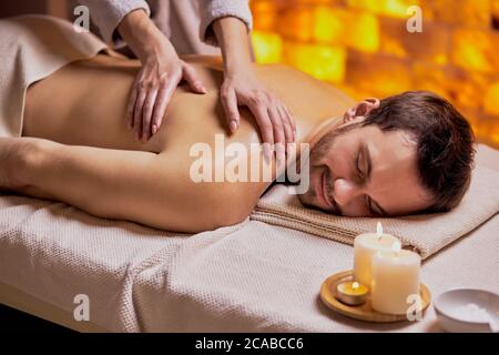 Young caucasian man relax during massage on back made by female hands, lying on spa table, enjoy spa treatment