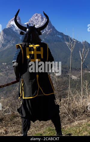 Japanese Samurai warrior dressed in armor with a mesmerizing mountainous background Stock Photo