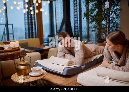 Young people look at each other happily after spa procedures, drinking green tea from teapot Stock Photo