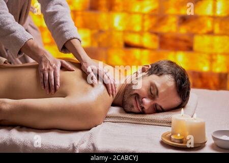 Young caucasian man relax during massage on back made by female hands, lying on spa table, enjoy spa treatment Stock Photo