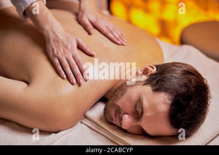 Young caucasian man relax during massage on back made by female hands, lying on spa table, enjoy spa treatment Stock Photo