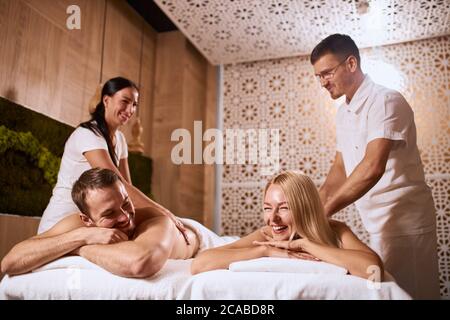 Charming young couple relaxing at beauty spa center, enjoying time together, receiving hand aroma therapy massage, lying on white towels, low angle sh Stock Photo