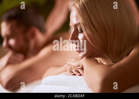 Close up of young beautiful lady with long blonde hair, resting on massage couch, keeps hands folded, putting head on hands, closed eyes with relaxati Stock Photo