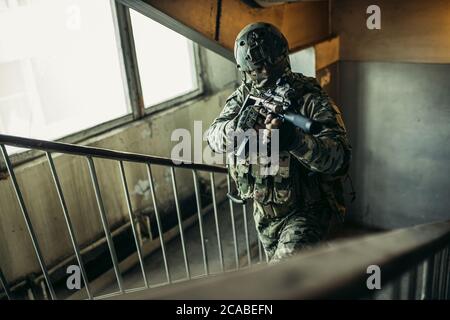 army and soldiers concept. soldier with weapon rifle in landing, climbing up the stairs, searching enemy to shoot, protect. Stock Photo