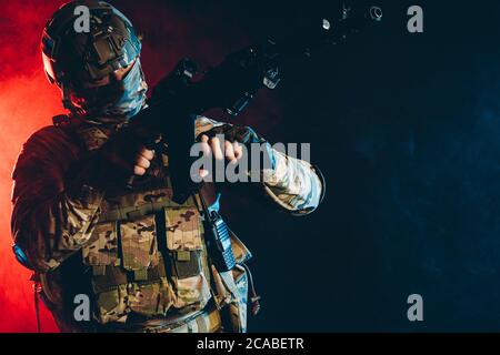 warrior military man wearing green uniform stand with gun rifle isolated over smoky background with ultra-violet rays, in search of enemy Stock Photo