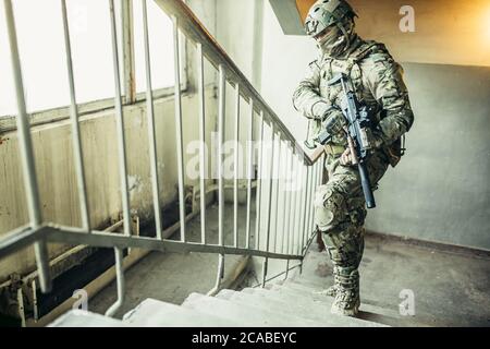 warlike soldier man goes up the stair looking for enemy or danger, holding weapon in hands, always ready to shoot Stock Photo