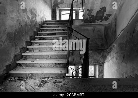Black and white image of stairway covered in rubble, mold and stains on the walls. Abandoned building located on Monte Grappa (Veneto, Italy) Stock Photo