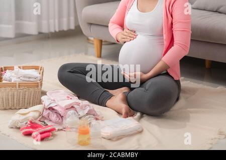 Beautiful pregnant asian woman packing and preparing baby clothes in basket for expectant new born baby Stock Photo