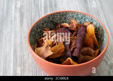 Sweet potato, beetroot and parsnip crisps chips in a patterned bowl.  Grey wood background Stock Photo