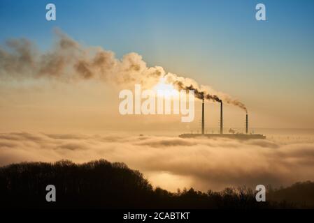 Horizontal snapshot of industrial area at setting sun, three smoking pipes from thermal power station pollute the atmosphere with black smog, concept of man-made disaster, environmental pollution Stock Photo