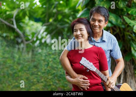 Middle aged  couple playing guitar while relax sitting on bench in backyard. Stock Photo