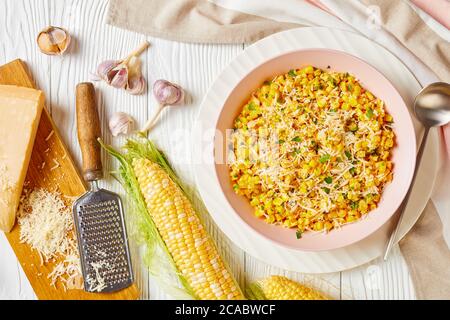 Parmesan Cilantro Corn in a pink bowl on a white wooden table with ingredients, horizontal view from above, flat lay, free space Stock Photo