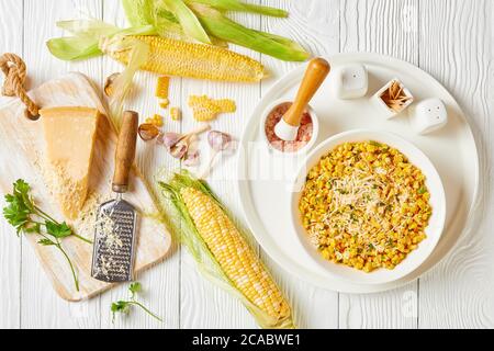 Parmesan Cilantro Corn in a white bowl on a white wooden table with ingredients on a white wooden table, horizontal view from above, flat lay Stock Photo
