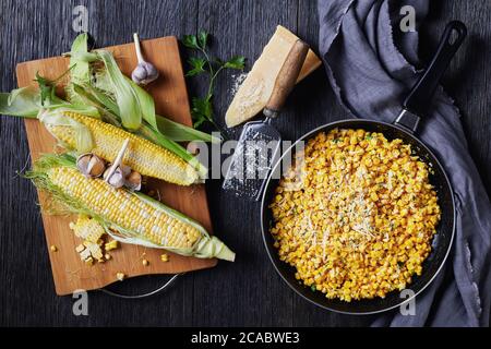 Parmesan Cilantro Corn in a skillet on a dark wooden table, horizontal view from above, flat lay, free space, Stock Photo