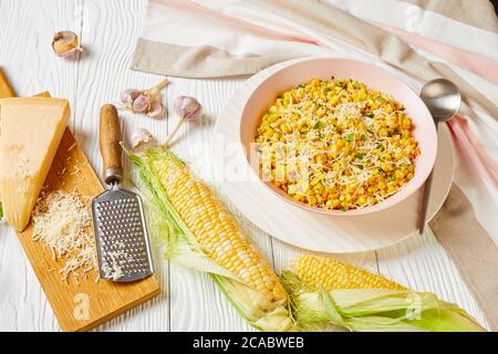 Rancho Parmesan Corn in a pink bowl on a white wooden table with ingredients, horizontal view from above, Stock Photo