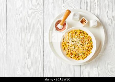 Parmesan Cilantro Corn in a white bowl on a white wooden table, horizontal view from above, flat lay, free space Stock Photo
