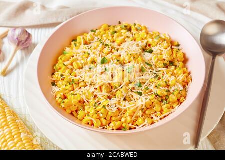 Parmesan Cilantro Corn in a pink bowl on a white wooden table with ingredients, landscape view from above, close-up Stock Photo