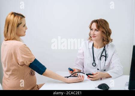 Smiling female doctor measuring young pregnant woman patient pulse pressure by hands Stock Photo