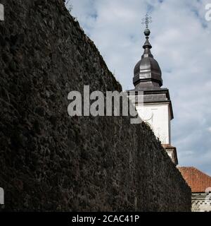 a white church tower behind an old mossy wall with a cloudy background Stock Photo