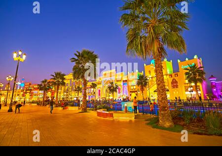 DUBAI, UAE - MARCH 5, 2020: The palm alley sretches along the canal of Global Village Dubai in front of the brightly illuminated trade pavilions of di Stock Photo
