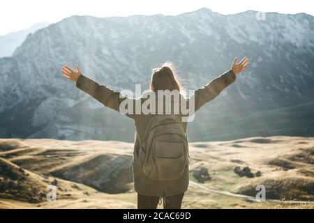 Young beautiful girl tourist or traveler alone on the background of a mountain landscape in autumn. She raised her hands and shows how happy and free she is. Stock Photo
