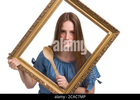 A young girl with long hair in a blue dress. Isolated on a white background. holding a wooden spoon, looking through the picture frame Stock Photo
