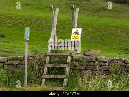 Bull in field warning sign attached to a ladder stile leading to a public footpath over a drystone wall.   Horizontal.  Space for copy. Stock Photo