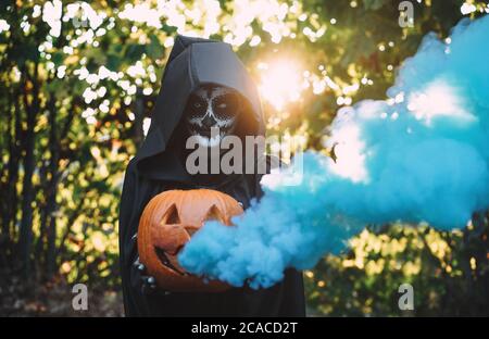 Girl with halloween costume and make up, holding a pumpkin with a smoke bomb inside - Holidays, party, scary and autumn concept - Focus on face Stock Photo