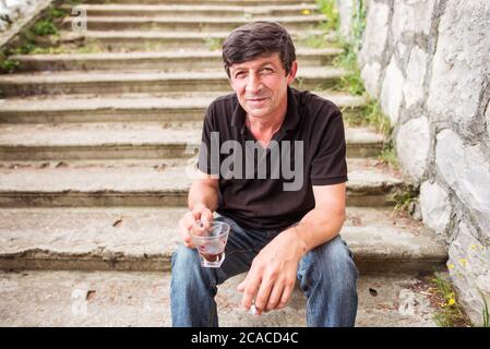 Sukhumi / Abkhazia - August 2, 2019: russian ethnic man drinking coffee and smoking cigarette sitting on old stairs Stock Photo