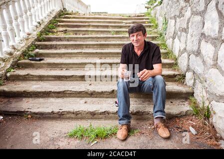 Sukhumi / Abkhazia - August 2, 2019: russian ethnic man drinking coffee and smoking cigarette sitting on old stairs Stock Photo
