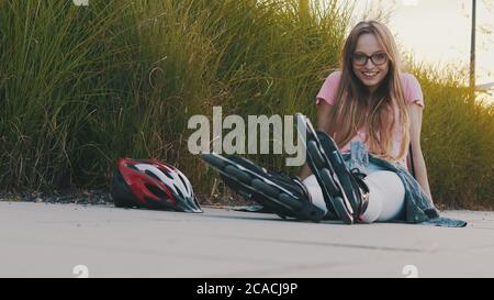 Young caucasian woman siting on the trail in the park with rollerblades during the sunset. Sport and recreation concept. High quality photo Stock Photo
