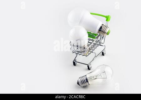 The concept of modern economical lighting. Energy-saving light bulbs are placed in a basket on wheels. A simple light bulb is lying on the table. Stock Photo